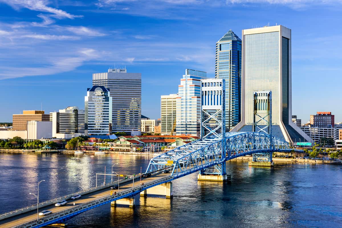 The blue steel Main Street Bridge carrying traffic over the St Johns River in Jacksonville, Florida, with the downtown skyline rising behind its two lift towers